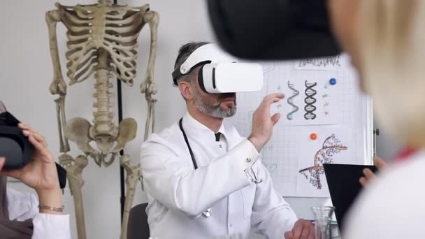 Médecin attentionné attrayant avec des cheveux gris et barbe portant des lunettes de réalité virtuelle effectuant une procédure médicale expérimentale dans le bureau de l'hôpital — Video