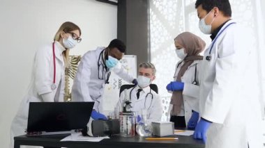 Klinikte mikroskopla çalışan yoğun ırk doktorları ve meslektaşlarıyla birlikte uzman bir doktor.