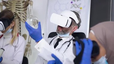 Saygıdeğer gri sakallı doktor kimyasal maddeyi sanal gerçeklik kulaklığı kullanarak matarada öğreniyor.