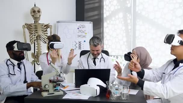 Уважаемый симпатичный седовласый врач-наставник, управляющий работой своих врачей-интернов, которые носят очки виртуальной реальности — стоковое видео