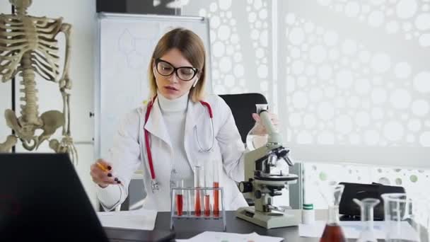 Trabajadora médica femenina atractiva concentrada escribiendo marcas durante su trabajo con relleno de frasco de líquido transparente — Vídeo de stock