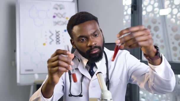 Geconcentreerd ervaren Afro-Amerikaanse arts vergelijkt twee reageerbuizen met vloeistoffen in het ziekenhuis laboratorium — Stockvideo
