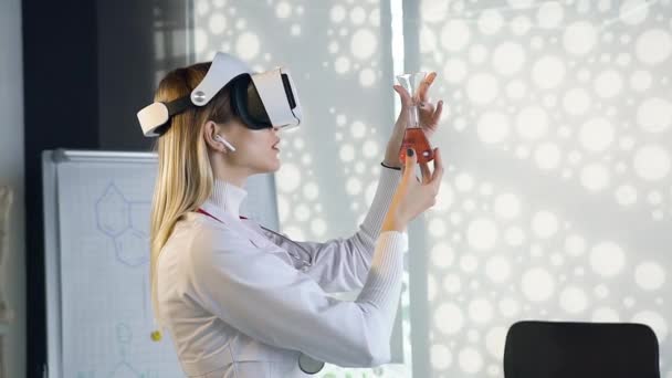 Attractive portrait of high-skilled concentrated female scientist in white gown which working with flask with chemical solution using virtual reality headset — Stock Video