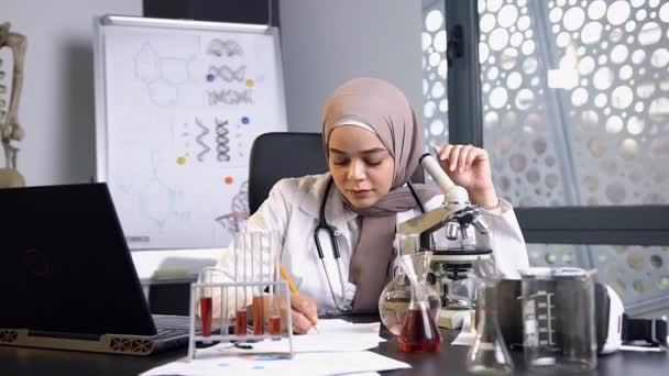Visão aproximada da bela médica concentrada no hijab que trabalha com tubo de ensaio com líquido químico em laboratório médico — Vídeo de Stock