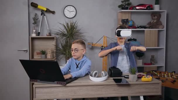 Mouvement lent de deux garçons adolescents qui jouent ensemble sur des jeux vidéo en utilisant un casque de réalité virtuelle et un ordinateur dans la salle de jeux — Video