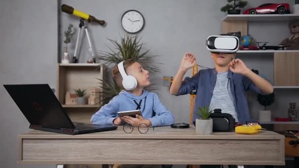 Close view of satisfied teen boys which enjoyng leisure using virtual reality goggles and tablet in playroom — Wideo stockowe