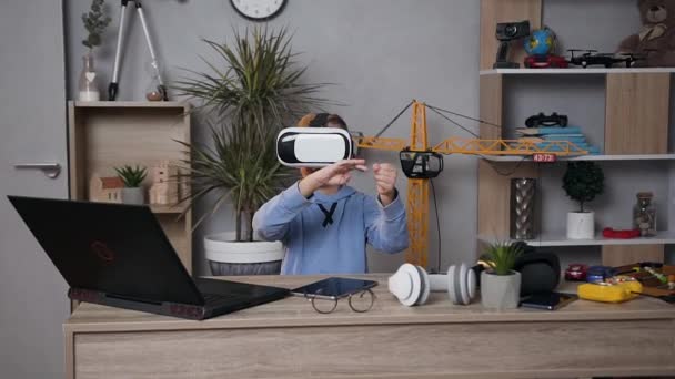 Moderne slimme 5-7 leeftijd jongen zitten aan de tafel in de kinderkamer en met behulp van virtual reality headset speelt video game — Stockvideo