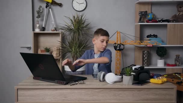 Ελκυστικό πορτρέτο του σύγχρονου όμορφου έφηβου αγοριού που κάθεται στο τραπέζι και επιλέγει το παιχνίδι στον υπολογιστή και στη συνέχεια χρησιμοποιώντας γυαλιά επαυξημένης πραγματικότητας — Αρχείο Βίντεο
