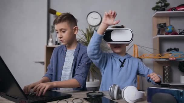 Joyful goed uitziende tiener broers genieten van video game met behulp van augmented reality bril en computer — Stockvideo