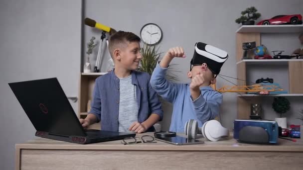 Χαρούμενα ικανοποιημένα έφηβα αγόρια-φίλοι που παίζουν βιντεοπαιχνίδια μαζί χρησιμοποιώντας υπολογιστή και γυαλιά επαυξημένης πραγματικότητας — Αρχείο Βίντεο