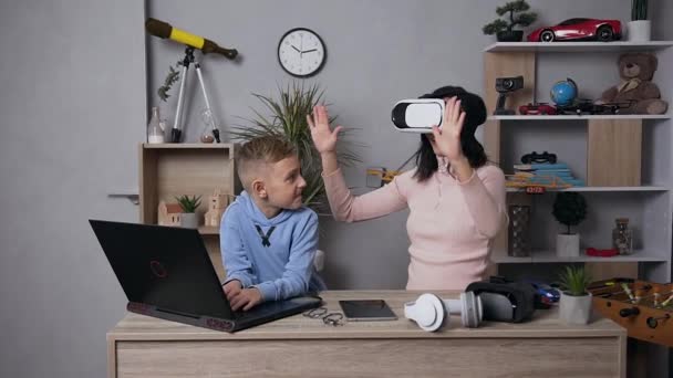 坐在虚拟3D眼镜上的漂亮的黑发女人和10岁的儿子在家里用电脑微笑的场景 — 图库视频影像
