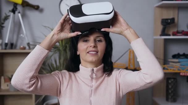 Bonita morena sonriente mujer mirando a la cámara y poniéndose gafas 3D virtuales especiales y haciendo movimientos de manos en el aire en casa — Vídeos de Stock