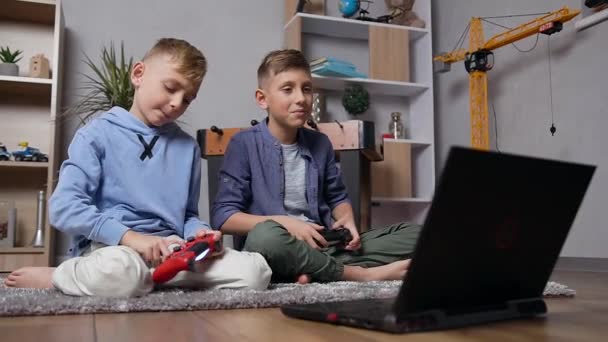 Seitenansicht von zwei gutaussehenden, modernen Teenagern, die auf dem Teppich sitzen und emotional Videospiele am Computer mit Joysticks spielen — Stockvideo