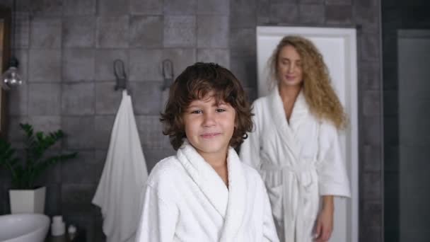 Portrait shot of a lovely little boy in a white coat who is standing in the bathroom while his beloved mother comes to him and hugs him — Stock Video