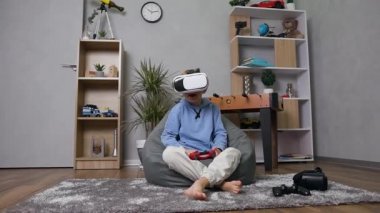 Yakışıklı, 10 yaşında bir çocuk şişme kanepeye oturmuş özel sanal 3D gözlükler kullanarak joystick 'le oyun oynuyor.