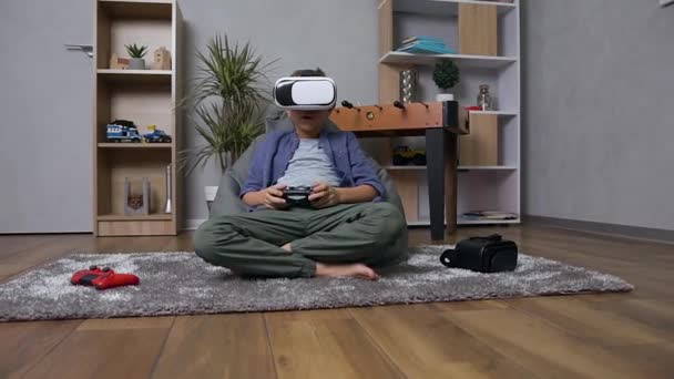 Snygg modern 12-årig pojke sitter på uppblåsbar fåtölj spela TV-spel med hjälp av gamepad och bär virtuella 3D-glasögon — Stockvideo