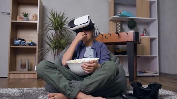 Vista frontal de niño moderno concentrado y atractivo que se sienta en el sillón inflable y come palomitas de maíz durante la visualización de vídeo utilizando gafas 3D virtuales — Vídeos de Stock