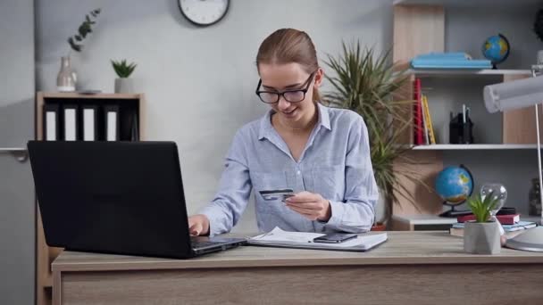 Espléndida joven alegre utilizando la computadora y su tarjeta bancaria para hacer el pago en línea para la compra — Vídeos de Stock