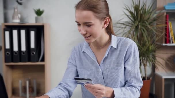 可爱的微笑25岁的女人坐在桌旁，用笔记本电脑和信用卡在网上购物 — 图库视频影像