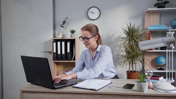 テーブルに座ってコンピュータと仕事をする眼鏡の豪華な幸せな若い女性の魅力的な肖像画 — ストック動画