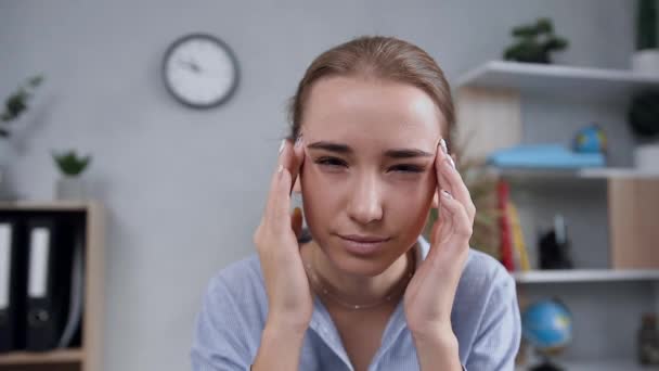 Chica rubia atractiva infeliz masajeando los templos para aliviar el dolor de cabeza durante su trabajo en la computadora en el gabinete moderno — Vídeos de Stock