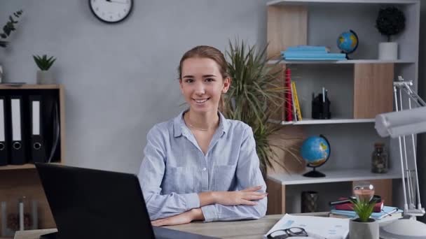 Auto-assurée splendide jeune femme blonde assise à la table et regardant la caméra avec un sourire mignon — Video