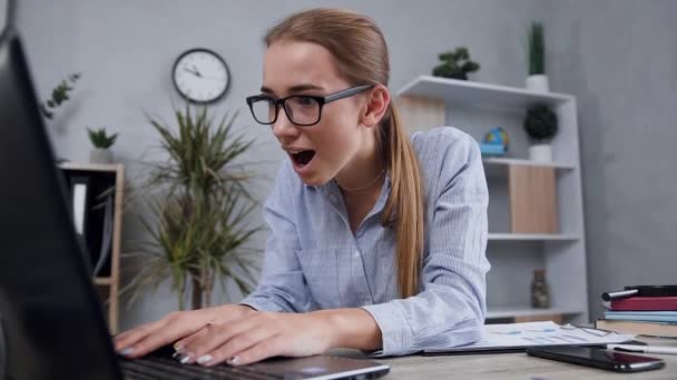 Überrascht gut aussehendes blondes Mädchen mit Brille, das auf den Computerbildschirm blickt und vom Ergebnis lächelt — Stockvideo
