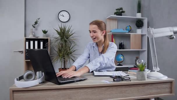 Vista cercana de la encantadora dama sonriente asombrada que se sienta en su lugar de trabajo y satisfecha de los buenos resultados vistos en la computadora — Vídeos de Stock