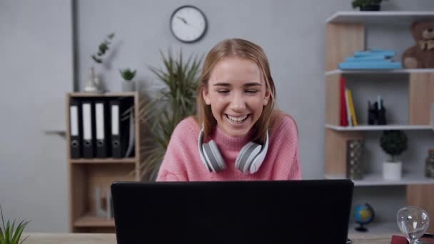 Vue de face de jeune fille blonde attrayante à l'esprit aigu en pull rose qui regarde moniteur et souriant sincèrement — Video