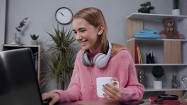 Oldukça neşeli, modern, şık kazaklı bir kadın bilgisayarın başında oturmuş komik videoların keyfini çıkarıyor.