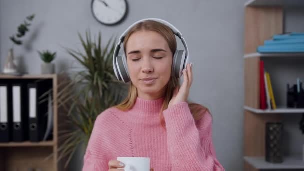 Piacevole bella signorina in elegante maglione indossando cuffie ascoltare bella musica sul suo posto di lavoro — Video Stock