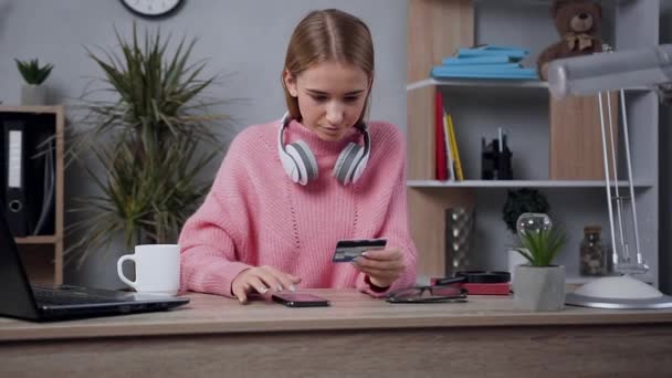 Привлекательная улыбающаяся блондинка в модном свитере делает покупки в интернете, используя свою кредитную карту и смартфон — стоковое видео