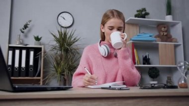 Çayı içip deftere bir şeyler yazan pembe kazaklı çekici, modern bir kız.