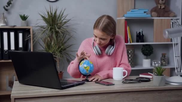 Bella giovane bionda sorridente vestita con maglione rosa lavorato a maglia che gira il piccolo globo e digita sulla tastiera — Video Stock