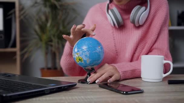 Close view of charming modern young woman in pink sweater which sitting at the table and spinning the small globe — 비디오