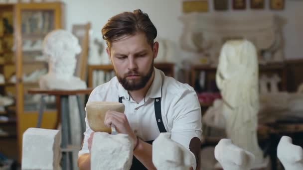 英俊而自信的现代大胡子石匠在工作室里用木槌、凿子和石灰石做工作 — 图库视频影像