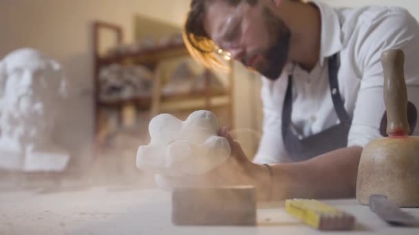 Netjes vriendelijke bebaarde beeldhouwer die in zijn atelier werkt met polijstgereedschap en handgemaakte figuur van krijt-steen — Stockvideo