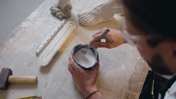 Aantrekkelijk portret van onbekende bebaarde beeldhouwer in beschermende glazen die mengsel mengen in kom — Stockvideo