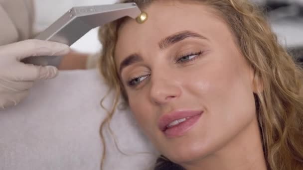 Concept de beauté où splendide femme blonde satisfaite rafraîchissant son visage à l'aide de peeling aux ultrasons dans le salon de spa — Video