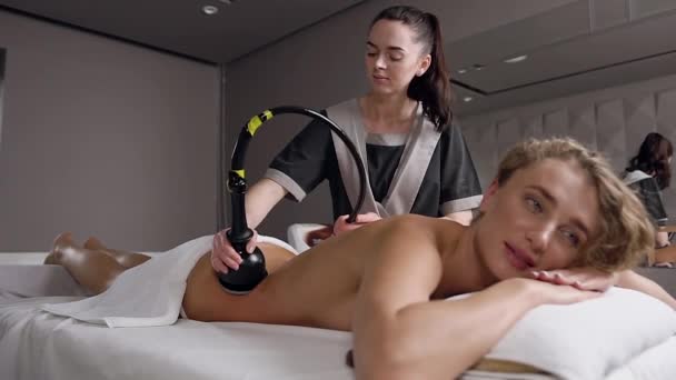 Mooie volwassen blonde vrouw liggend in op massage tafel en het hebben van anticellulite rug massage die vrouwelijke masseur doen met speciale tool — Stockvideo