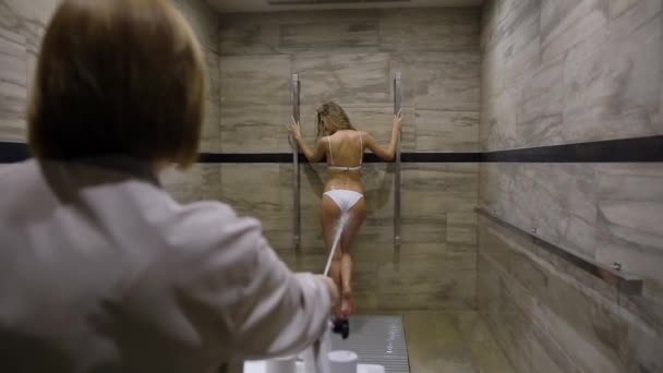 Радісна блондинка в купальнику насолоджується душем Шарко в спеціально обладнаній ванній кімнаті в спа-салоні. — стокове відео