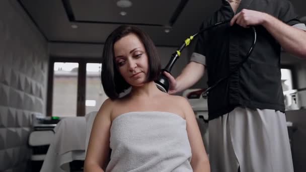 Ελκυστική σκούρα μαλλιά γυναίκα λαμβάνοντας μασάζ στο λαιμό με ειδικό ηλεκτρικό εργαλείο στο σαλόνι σπα — Αρχείο Βίντεο