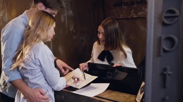 Happy amorous 30s couple looking on the places on map which showing for them smiling dark hair female manager at the reception desk — 비디오