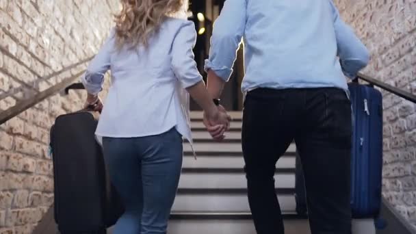 Back view of happy modern young couple with suitcases which running upstairs in contemporary hotel — 비디오