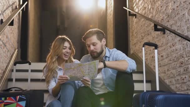 Långsam rörelse av snygga glada 30-tals par i kärlek som sitter på trappor och med hjälp av kartan talar om vackra platser de vill se — Stockvideo
