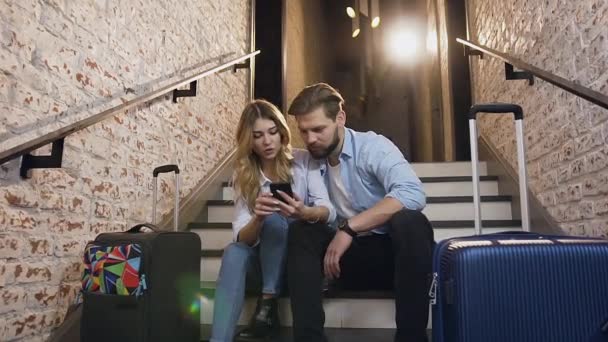 Hoş gülümseyen modern kadın ve erkek süslü tuğla duvarlı bir otelde merdivenlerde oturuyor ve telefon kullanıyor. — Stok video