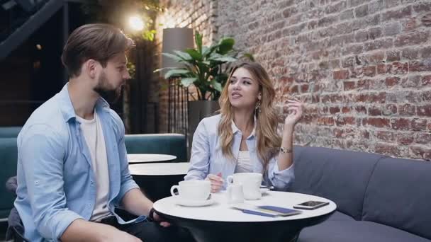Hezký vousatý muž sedí se svou šťastnou blond přítelkyní v hale a pije čerstvě uvařený čaj — Stock video