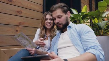 Good-looking elated modern young woman and man which sitting on soft couch in hotel hall and using tablet pc and map