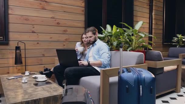 Atractiva pareja moderna joven sentada en el vestíbulo del hotel y mirando el ordenador — Vídeo de stock