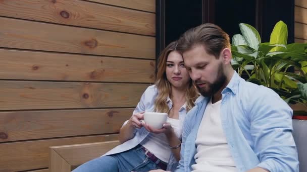Счастливая улыбающаяся современная пара сидит в уютном холле и смотрит на планшетный компьютер — стоковое видео